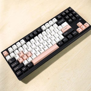 May include: A mechanical keyboard with a black frame and a mix of white, black, and light pink keycaps. The layout includes standard alphanumeric keys, function keys, and arrow keys. A small pulse icon is printed on the top right corner of the frame.