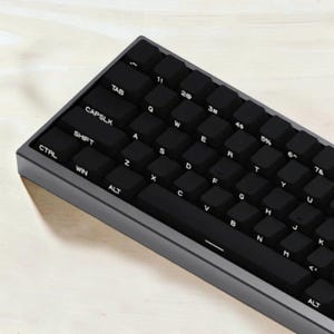 May include: A compact mechanical keyboard featuring a dark gray frame and black keycaps with white lettering. The layout includes standard QWERTY keys, a space bar, and modifier keys such as CTRL, WIN, ALT, SHIFT, TAB, and CAPSLK, all clearly labeled.