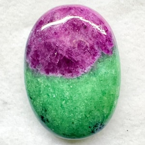 May include: An oval-shaped cabochon gemstone featuring a distinct color split. The upper portion is a deep, vibrant magenta-pink with a crystalline texture, while the lower portion is a bright, granular lime green with subtle dark inclusions.