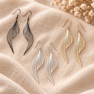 May include: Three pairs of dangle earrings featuring a delicate, open-work leaf or feather design with fine, curved lines. The set includes one pair in matte black, one pair in polished silver, and one pair in gold, all with hook-style ear wires.