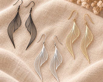 May include: Three pairs of dangle earrings featuring a delicate, open-work leaf or feather design with fine, curved lines. The set includes one pair in matte black, one pair in polished silver, and one pair in gold, all with hook-style ear wires.