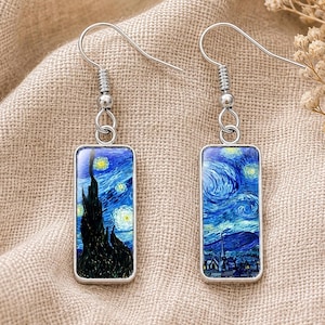 May include: A pair of silver-toned drop earrings featuring rectangular pendants. Each pendant displays a miniature reproduction of the Starry Night painting, showcasing swirling blue and yellow brushstrokes, a dark cypress tree, and a village scene.