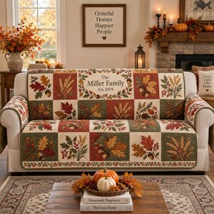 Könnte beinhalten: Ein rechteckiger Sofabezug mit einem Patchwork-Design aus Herbstblättern, Weizenähren und Eicheln in Grün-, Rot- und Goldtönen. Das mittlere Feld zeigt den Text 'The Miller Family Est. 2019', umgeben von einem dekorativen Kranz aus Blättern.