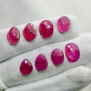 May include: Eight faceted loose gemstones in a vibrant magenta-pink hue. The collection includes four pear-shaped stones and four oval-shaped stones, all featuring a polished, multi-faceted surface that reflects light across their deep, saturated colour.