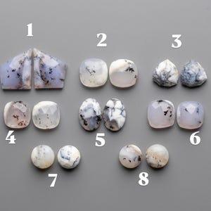 May include: Eight pairs of faceted and smooth dendritic opal gemstones arranged in rows, labelled 1 through 8. The stones feature translucent to opaque white and light blue hues with dark, fern-like inclusions. Each pair displays unique patterns.