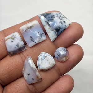 May include: A collection of six faceted dendritic opal gemstones featuring a translucent white and pale blue base with dark, fern-like inclusions. The stones vary in shape, including square, triangular, and circular cuts with polished surfaces.