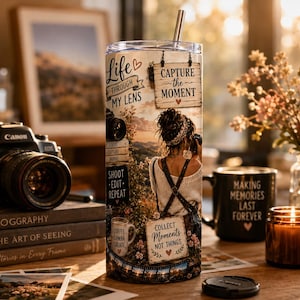 Könnte beinhalten: Ein zylindrischer Becher mit einem Fotodruck einer Person, die eine Kamera hält, sowie den Texten Life Through My Lens, Capture the Moment, Shoot Edit Repeat und Collect Moments Not Things, inklusive transparentem Deckel und Metallhalm.