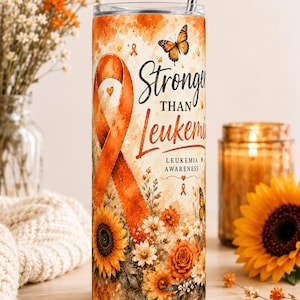 May include: A cylindrical stainless steel tumbler featuring an orange awareness ribbon, a monarch butterfly, and a floral arrangement of sunflowers and roses. The text reads "Stronger THAN Leukemia" and "LEUKEMIA AWARENESS" with a metal straw.