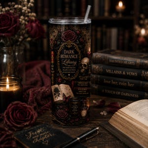 Op de afbeelding: Een hoge cilindrische beker met een doorzichtig deksel en een metalen rietje, voorzien van een donker, gotisch geïnspireerd ontwerp met gouden tekst Dark Romance Library, een schedel, een open boek, rozen en flesjes op een zwarte achtergrond.