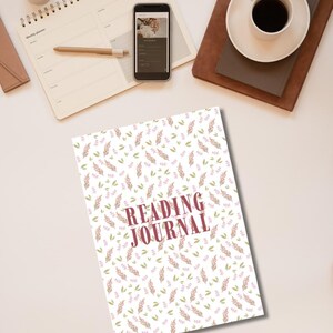 May include: A rectangular reading journal with a white cover featuring a repeating pattern of small pink floral sprigs and green leaves. The words READING JOURNAL are printed in large, bold, dark red capital letters in the center of the cover.