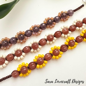 May include: Three beaded bracelets with a sunflower design. The bracelets feature brown, white, and yellow beads, with larger brown beads at the center of each flower. The bracelets are on a white surface. The text "Sara Lovecraft Designs" is at the bottom.