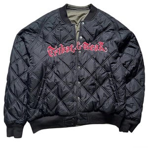 Könnte beinhalten: Eine schwarze, gesteppte Bomberjacke mit Rautenmuster sowie geripptem Kragen und Bündchen. Der Schriftzug Tribal Gear ist in roter, gotischer Schrift auf der Brust eingestickt. Die Jacke verfügt über einen durchgehenden Druckknopfverschluss.