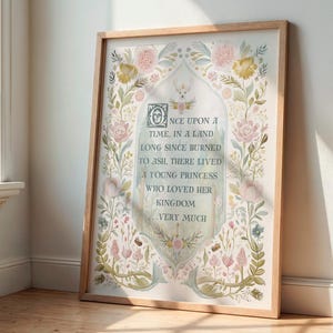 May include: A framed art print with a light wood frame. The artwork features floral and botanical illustrations in pastel colors, surrounding text that reads "ONCE UPON A TIME, IN A LAND...A YOUNG PRINCESS WHO LOVED HER KINGDOM...VERY MUCH."