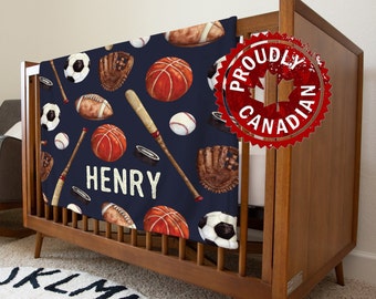 May include: A navy blue baby blanket with a sports theme. The blanket features a repeating pattern of baseball bats, baseballs, basketballs, soccer balls, and gloves. The blanket also has the name "HENRY" printed in white letters. The blanket is displayed in a crib with a wooden frame.