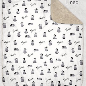 May include: White baby blanket with a repeating pattern of penguins and the name "Trevor" printed on it. The blanket is sherpa lined.