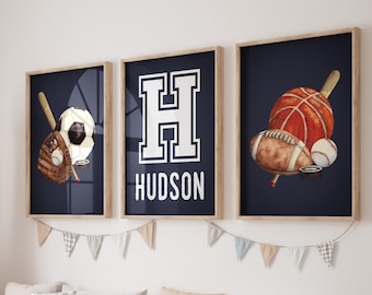 May include: Three framed prints with a navy blue background. The first print features a baseball glove, baseball, bat, and soccer ball. The second print features a large white letter H with the name "HUDSON" below it. The third print features a basketball, football, baseball, and hockey puck.