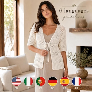 May include: A cream-colored, short-sleeved, open-front knit cardigan featuring a delicate lace-like pattern and a central tie closure. The garment is worn over a simple, solid-colored, light beige slip dress with thin shoulder straps.