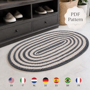 May include: An oval-shaped rug featuring concentric rings of alternating dark gray and cream-colored yarn. The rug has a textured, crocheted appearance with a repeating pattern of colors radiating from the center to the outer edge.