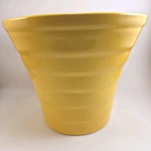 May include: A bright yellow ceramic planter with a wide, flared rim and a series of horizontal, rounded ridges encircling the exterior body. The vessel features a smooth, glossy finish that reflects light, creating a uniform, vibrant appearance.