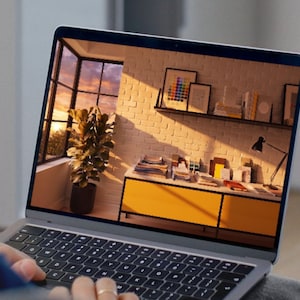 May include: A silver laptop with a black keyboard displaying a digital image of a room interior. The screen shows a yellow cabinet, a potted plant, a white brick wall, and a shelf with framed art and books illuminated by warm sunset light.
