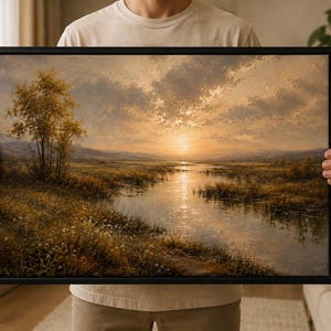 Op de afbeelding: Een rechthoekig landschapsschilderij in een zwarte lijst met een gouden zonsondergang boven een rustige rivier die door een grasweide slingert. De scène toont een opvallende boom op de linkeroever en warme amberkleurige tinten in het geheel.