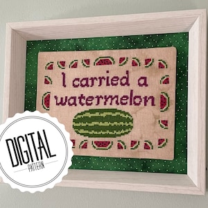 May include: A framed cross-stitch design with a green background and white polka dots. The cross-stitch features a watermelon and the text "I carried a watermelon".
