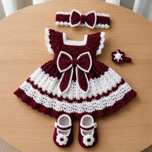 Può includere: Un vestito all'uncinetto bordeaux e bianco con un grande fiocco centrale, maniche con volant e scollo quadrato. Il set include una fascia per capelli all'uncinetto abbinata, un piccolo fermaglio floreale e due scarpine per neonati.
