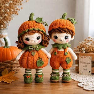 May include: Two crocheted dolls featuring pumpkin-themed outfits. The left doll wears a pumpkin-shaped hat and a skirt with green leaf accents. The right doll wears a pumpkin hat and orange overalls with green leaf details. Both have brown hair.