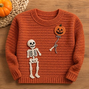 May include: A long-sleeve orange sweater featuring a crocheted white skeleton applique on the lower left and a crocheted orange jack-o'-lantern balloon applique on the upper right, connected by a grey string detail to the skeleton's hand.