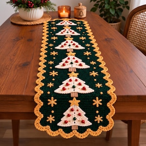 Op de afbeelding: Een donkergroene gehaakte tafelloper met een herhalend patroon van crèmekleurige kerstbomen met rode en groene kraalversieringen, bekroond met gele sterren, omringd door gele sneeuwvlokmotieven en een geschulpte gele rand.