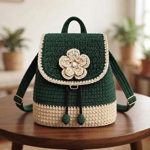 May include: A dark green crochet backpack featuring a beige base and a matching beige crochet flower embellishment on the front flap. The bag includes a top handle, adjustable straps with gold-tone hardware, and two black drawstring cords.