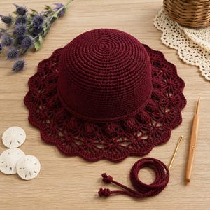 May include: A deep burgundy crochet hat with a solid crown and a wide, intricate lace-patterned brim. The set includes a matching burgundy yarn cord, a gold-toned metal needle, and a wooden crochet hook clearly marked with 3.5mm text.