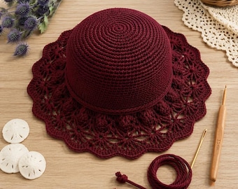 May include: A deep burgundy crochet hat with a solid crown and a wide, intricate lace-patterned brim. The set includes a matching burgundy yarn cord, a gold-toned metal needle, and a wooden crochet hook clearly marked with 3.5mm text.