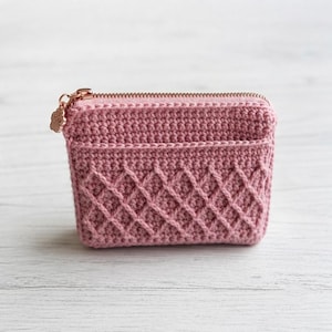 Può includere: Un portamonete all'uncinetto color rosa polvere con un motivo a rombi testurizzato sul pannello frontale. La pochette rettangolare è chiusa da una cerniera in metallo color oro rosa con un piccolo ciondolo a forma di zampa sul cursore.