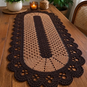 May include: An oval-shaped crochet table runner featuring a central dark brown panel surrounded by a tan border and a wide, scalloped dark brown edge with intricate openwork detailing. The runner displays a repeating geometric stitch pattern.