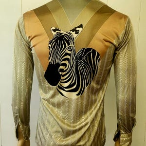 May include: A long-sleeved button-down shirt featuring a gold and silver herringbone pattern. The back displays a large, centered graphic of a black and white zebra head and neck, set against a V-shaped panel of solid gold fabric across the shoulders.