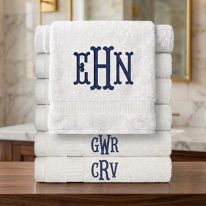 May include: A stack of six white cotton towels, each featuring navy blue embroidered monograms. The top towel displays the letters EHN, the second towel shows GWR, and the third towel features CRV, all in a decorative serif font style.