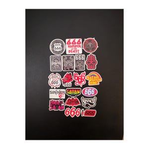 May include: A collection of various stickers featuring occult and dark themes, including text like 666, Number of the Beast, Sinner, and Satan Loves Me. The designs incorporate red, black, white, and rainbow colors in shapes like shields, circles, and rectangles.