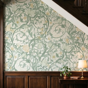 May include: Wallpaper featuring a repeating pattern of sage green swirling vines and pale yellow flowers on a cream background, installed above dark wood wainscoting in a room with a small wooden table, a potted plant, and a lamp.