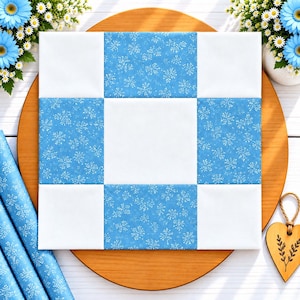 Può includere: Un blocco per trapunta quadrato con un motivo a griglia a nove riquadri. Il design alterna quadrati di tessuto bianco tinta unita a quadrati di tessuto blu decorati con un motivo botanico ripetitivo bianco simile a fiori o fiocchi di neve.
