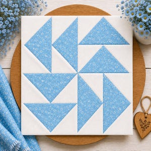 Peut inclure: Un bloc de courtepointe carré présentant un motif de moulinet composé de tissu blanc et de tissu bleu clair avec un petit imprimé floral blanc. Le design se compose de huit triangles disposés pour créer une forme géométrique rotative.