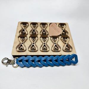 Peut inclure: Un dé en bois avec des découpes en forme de sablier, une pièce de cuir en forme de cœur avec le texte "TOPHOME" et un porte-clés en cuir bleu avec un fermoir en métal. Le dé est brun clair et le porte-clés est bleu vif.