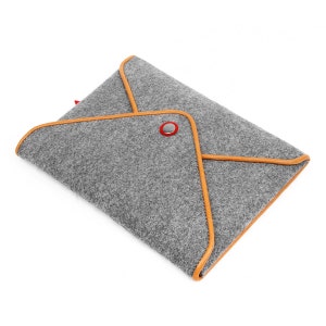 Peut inclure: Pochette pour ordinateur portable en feutre gris avec une bordure en cuir marron et une fermeture à bouton rouge.