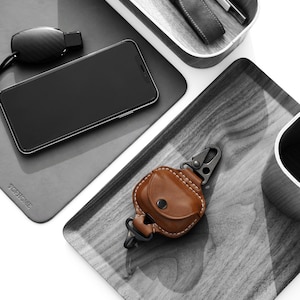 Op de afbeelding: Een set van drie grijze houten trays met een zwarte telefoon, een zwarte fluit, een bruine leren sleutelhanger met een metalen karabijnhaak en een zwart-wit logo met de tekst "TOPHOME Simple Design Simple Life".