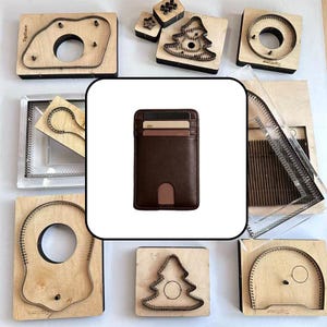 May include: A dark brown leather card holder with multiple slots containing three cards, surrounded by various wooden and metal craft cutting dies of different shapes including a Christmas tree and circular patterns on a white background.