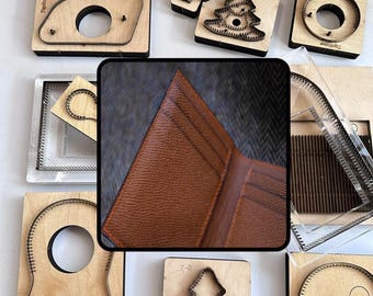 May include: A brown leather wallet with visible card slots and textured grain, centered over a collection of various wooden and metal cutting dies for leathercraft, including shapes like circles, trees, and geometric frames with metal blades.