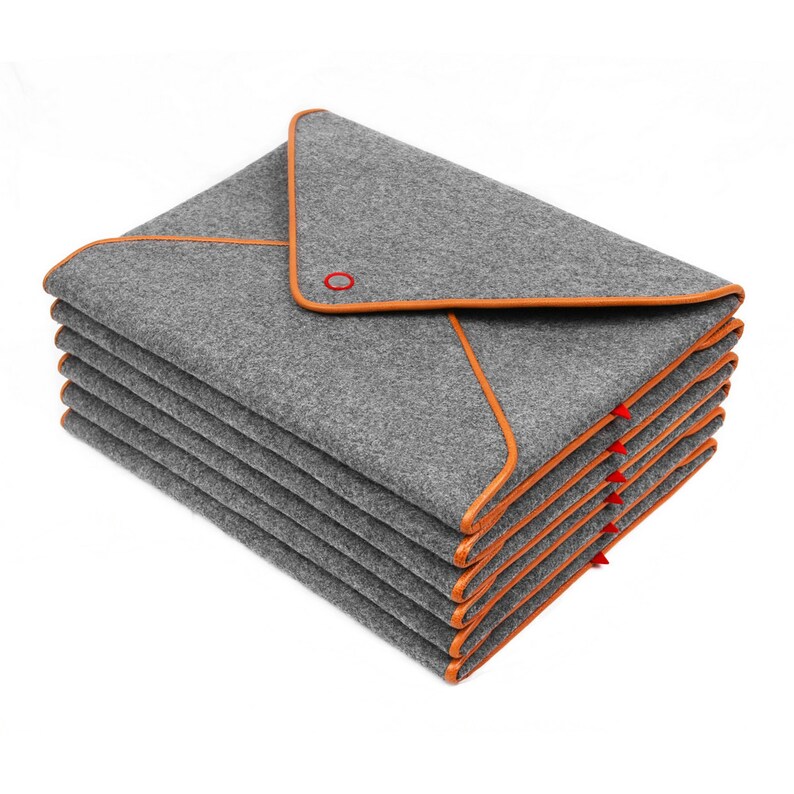 May include: A stack of grey felt blankets with orange trim. Each blanket is folded into a triangular shape. A red grommet is visible on the top blanket. The blankets are neatly stacked, showcasing the orange trim.