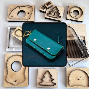 Könnte beinhalten: Eine Auswahl an Lederhandwerkzeugen und eine teal-farbene Ledergeldbörse. Die Werkzeuge umfassen verschiedene Metallstanzformen auf Holzblöcken, mit Formen wie Kreisen, einem Weihnachtsbaum und anderen geometrischen Designs. Die Geldbörse hat einen Druckknopfverschluss und grüne Nähte.