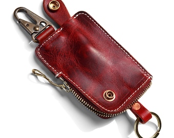 May include: A red leather key holder with a zipper closure and a metal hook. The key holder has a distressed look and is accented with brass hardware.