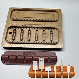 May include: An image of cable organisers and molds. The image shows a brown leather cable organiser with the text "TOPHOME" and an orange cable organiser with several white cables. Also shown are two wooden molds with the text "TopHome".